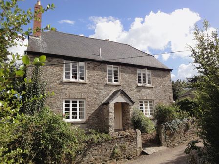 A stone house with six white windows and a small porch surrounded by green shrubs at Maristow Barton in Milton Combe near Lopwell Dam