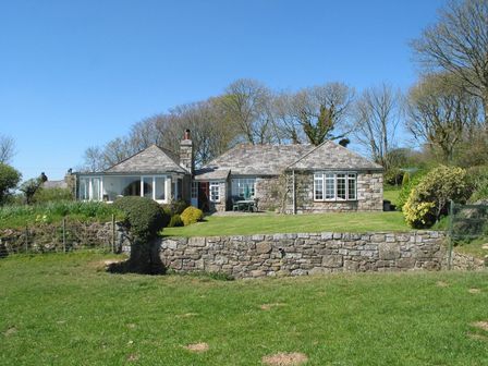 A stone house with a tiled roof and a lawn in front surrounded by trees at Higher Tumrose in Blisland