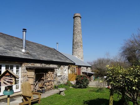 A stone building with wood stacks and a tall chimney in a garden at The Old Engine House in Tretoil near Bodmin