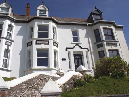 The front exterior of a white house with bay windows and a black door at Heightley House in Treknow near Tintagel