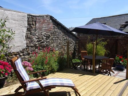 An outdoor patio area with wooden lounge chair and table with umbrella surrounded by plants at Millers Cottage in Bude