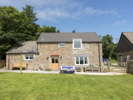 A stone cottage with wooden door and windows a lawn and benches at Salty Cottage in Morwenstow