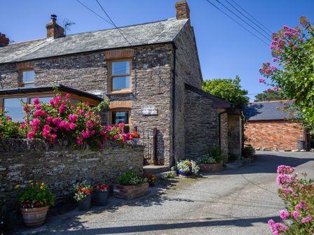 A stone cottage with flower pots and pink flowers outside Uphill Cottage in Penrose near St Merryn