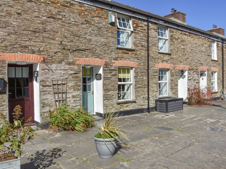 A stone terrace with potted plants and multiple cottage doors and windows at Primrose Cottage in Edmonton near Wadebridge