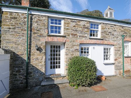 Stone cottage exterior with white doors and windows a green bush and blue sky at Grooms Cottage in St Minver near Polzeath