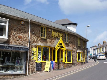 A street with shops including a jewellers and a store with yellow window frames and signage at The Workshop in Bude
