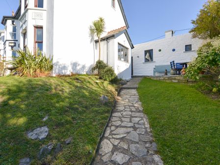 A stone pathway leading to a white house with a small garden and outdoor seating area at Heatherdale in Treknow near Tintagel