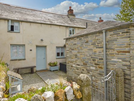 Exterior of a stone and stucco house with a blue door and windows a stone path and garden at 3 Newhall Green in St Teath