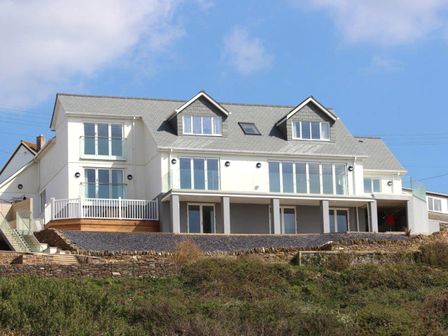 A large two-story house with a gray roof and multiple windows on a hillside at Seagulls Perch in Mawgan Porth
