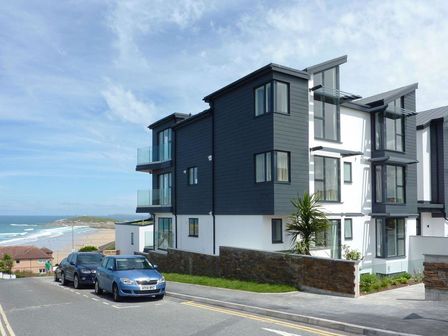 Modern housing complex near a beach with parked cars and a blue sky at Rosen in Newquay