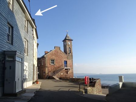 A stone clock tower near the sea with buildings on the left and a clear sky at Nirvana in Kingsand And Cawsand
