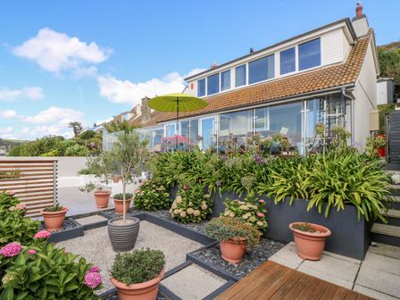 A garden area with potted plants and a green umbrella outside a house with large windows at Rock Rose in Downderry
