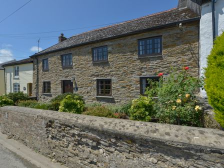 A stone cottage with a garden and a low stone wall in front at Samuels Cottage in Lanreath