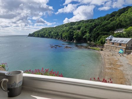 A view of a beach and calm sea with green hills and a building near the shore at Balcony Cottage in Kingsand And Cawsand