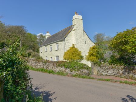 A stone house with chimneys behind a stone wall and gate along a country road at Tregonhawke Farmhouse in Millbrook