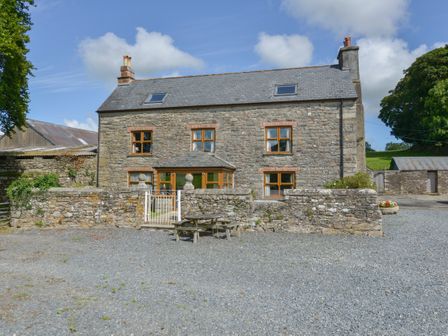 A stone house with six windows and two chimneys surrounded by a stone wall and a gravel yard at Haye Barton Farm in St Ive