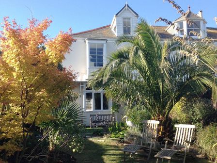 A garden with trees and two wooden chairs in front of a white house at 1 Florence Place in Falmouth