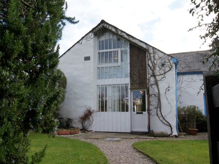 A white cottage with a gravel pathway and greenery at Regatta Cottage in Feock