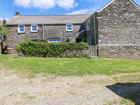 An exterior view of a stone farmhouse with multiple windows a wooden gate and a grassy lawn at Polcreek Farmhouse in Veryan