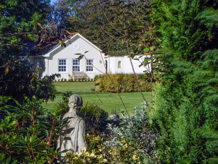 A garden with a stone statue and bushes looking towards a white house at Charlton Lodge in Mawnan Smith