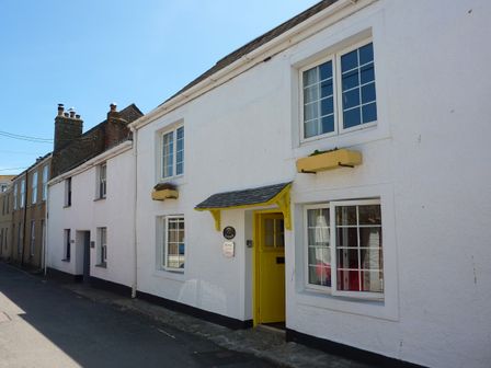 A white cottage with yellow door and window boxes on a narrow street at April Cottage in Coverack