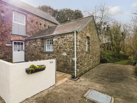 A stone cottage with a small white wall and a garden area at Badger Cottage in Mawgan-in-Meneage near Helston