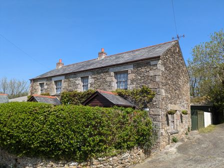 A stone cottage with a slate roof and chimneys surrounded by greenery at Swift Cottage in Mawgan-in-Meneage near Helston