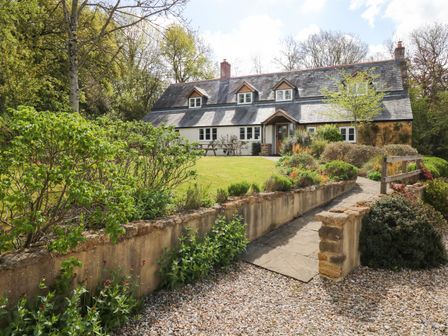 A stone pathway leads to a white house with a slate roof surrounded by trees and garden at Marles Farmhouse in Salwayash