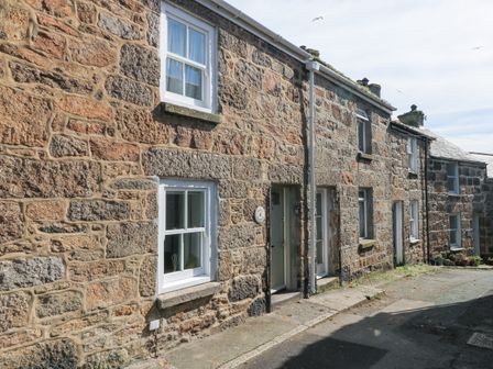 Stone terrace houses with white window frames on a paved street at Mural Cottage in Mousehole