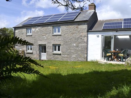 A stone house with solar panels on the roof and a patio table with chairs in a garden at The Studio in Rinsey Cove near Praa Sands