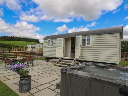 An outdoor patio area with a small shepherd's hut, hot tub, metal table and chairs with flowers on a table and a potted plant at Hillside View in Rhayader