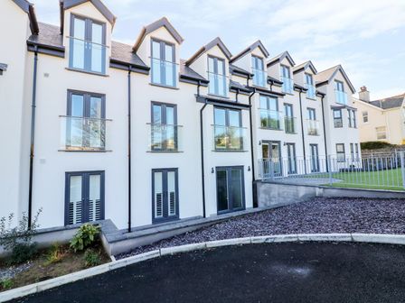 The exterior of a modern three-story white residential building with black-framed windows and glass railings at 6 Bay View in Benllech