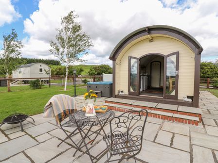 An outdoor patio with a metal table and chairs a small building with open doors and green grass at Mountain View in Rhayader