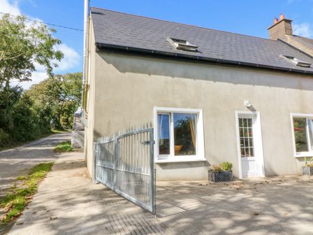 Exterior view of a house with a gray gate driveway and two windows beside a door at Beehive Cottage in Kilbrittain County Cork