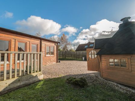 An outdoor area with a wooden building and a small wooden cabin with a gravel ground and a wooden fence at Sunnyside Lodge in Crewkerne