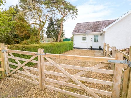 A gravel driveway with a wooden gate and a white house in the background at 4 Hanbury Lodge in Pentlepoir