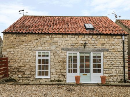 Stone cottage with tiled roof windows and a glass door with two plant pots outside at The Bothy 21 West Street in Swinton near Malton