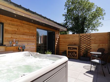 An outdoor patio with a hot tub wooden wall a table and two chairs and a wood storage unit at The Stables in Cross Keys near Hereford