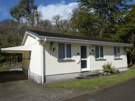 A single story house with white walls surrounded by trees and shrubs at Little Retreat in Liskeard