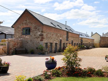 A stone and brick barn with multiple windows and doors surrounded by potted plants and flowers at Swifts Barn in Brixham