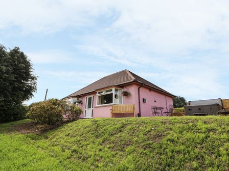 A pink bungalow house with a bench and outdoor table on a grassy hill at Tegfan in St Harmon