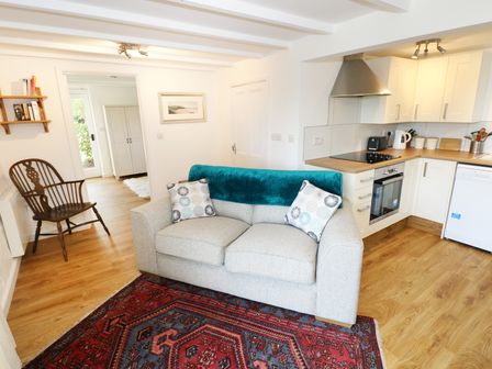 A living room with a sofa and kitchen area with white cabinets and appliances at The Granary Cottage in Llangrannog near Cardigan