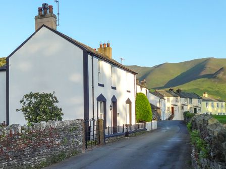 A row of white houses along a narrow paved road with stone walls and green hills in the background at Dale House in Lorton
