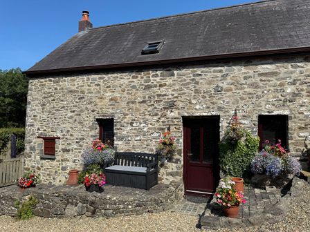 An outdoor area with a stone wall and flowers at Old Farmhouse Cottage New Quay