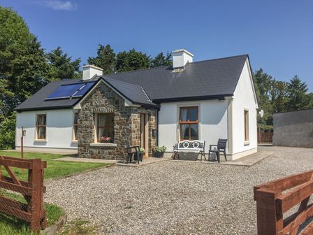 A cottage with white walls and a stone porch surrounded by trees and a gravel driveway at Cloonkee Cottage in Ballina County Mayo