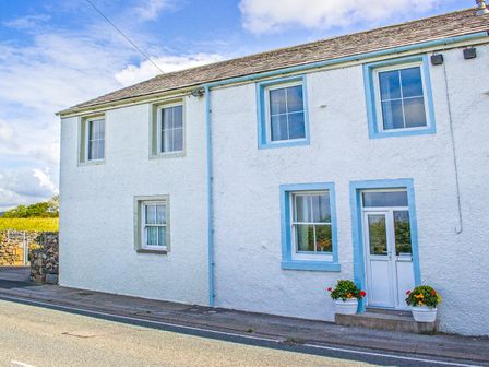 White exterior of a house with four windows, a door with blue trim, and two flower pots on the doorstep at 2 Park Nook Close in Waberthwaite