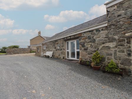 An exterior view of a stone building with a bench and potted plants at Coetsiws Clynnog Fawr