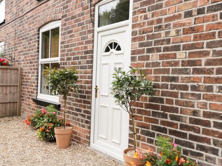 A brick house exterior with a white door numbered 2 two potted plants and flower beds at 2 Moor Farm Cottages Hornsea
