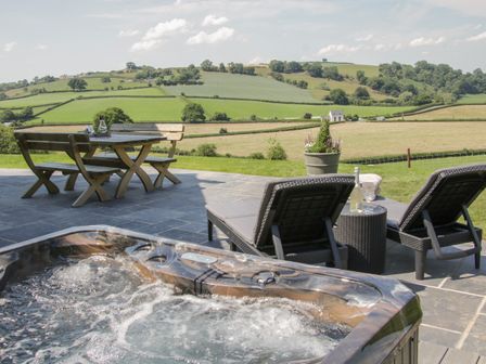 An outdoor patio with a hot tub wooden table with benches and two lounge chairs overlooking green fields at Shepherd's Rest in Montgomery