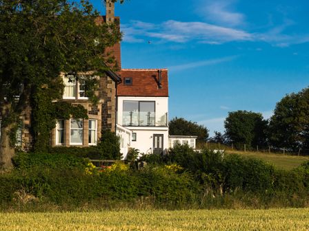 A stone and white house with a balcony overlooking a field and trees at Emblestones in Embleton
